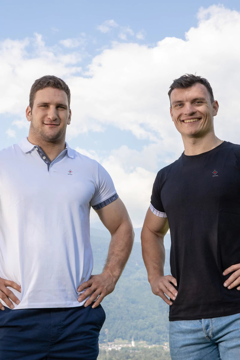 Zwei Männer tragen Edelvetica Shirts in Weiss und Schwarz, posieren vor imposanter Schweizer Bergkulisse – Symbol für Stärke, Qualität und Swiss Made Mode