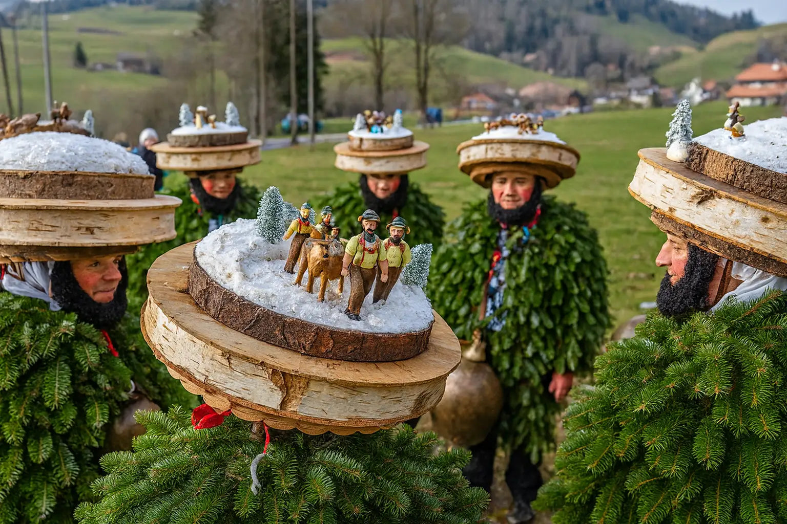 Teilnehmer in traditionellen Tannenkostümen beim Silvesterchlausen im Appenzell, mit kunstvoll geschnitzten Holzhauben und Miniaturszenen auf verschneitem Hintergrund, vor alpiner Landschaft.