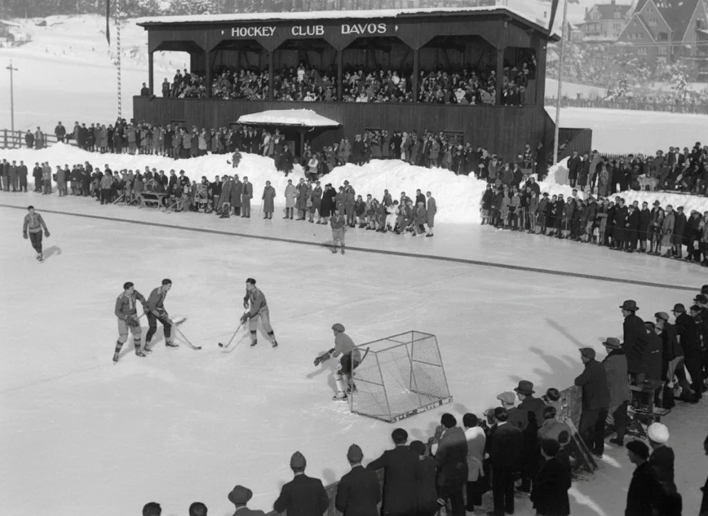 Historisches Schwarz-Weiß-Foto eines Eishockeyspiels beim Spengler Cup Davos in den frühen Jahren mit Zuschauern und Holztribüne