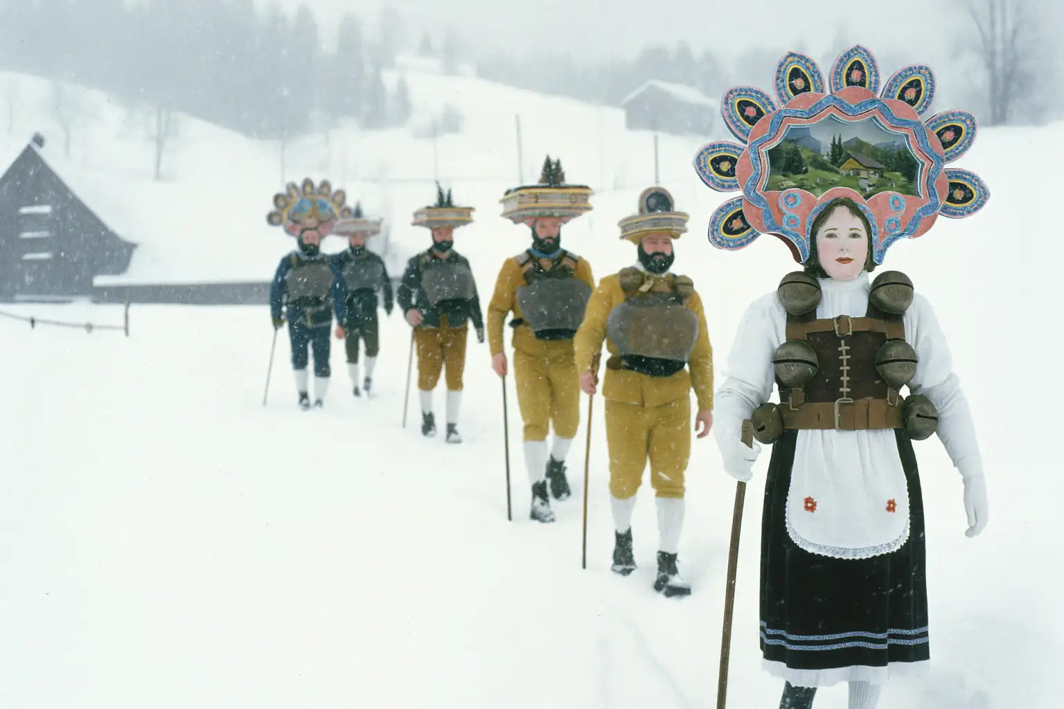 Silvesterchläuse in farbenprächtigen Kostümen mit Glocken und kunstvollen Hüten beim Umzug durch verschneite Appenzeller Landschaft